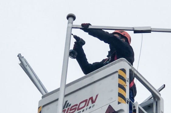 Technicien de service montant une potence sur un mât à drapeau depuis la nacelle