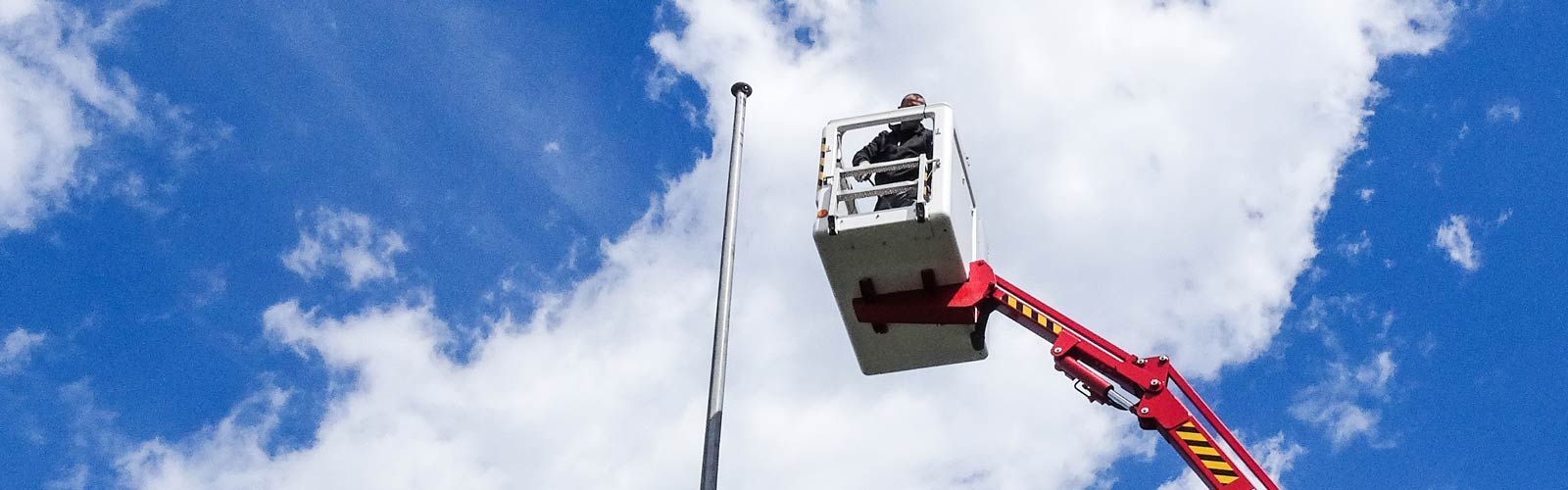 Technicien de service de Mastservice.ch sur la nacelle à côté d'un mât à drapeau